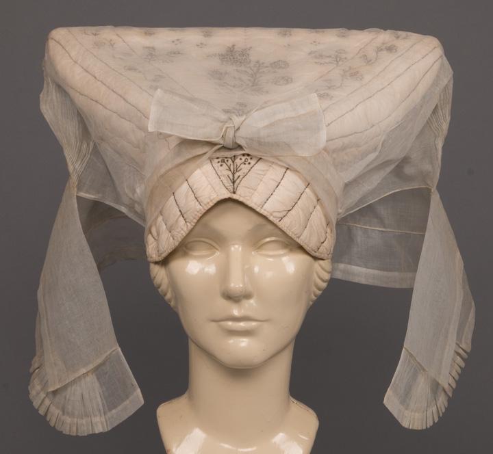 REGIONAL HEADDRESS, FRANCE, c. 1845: French regional headdress in white quilted cotton w/ black floral embroidery to crown & organdy over drape gathered to ribbon closure at back neck & secured w/ bow, (very light spot stain & fugitive d