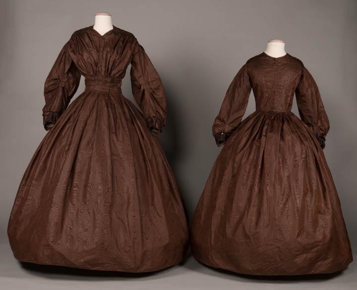 MOTHER & DAUGHTER AFTERNOON DRESSES, AMERICA, 1840s: Brown silk moire mother, late 1840s, roller stamped silk moire, W doubled box pleated at front, back w/ deep cartridge pleating, corded hem, black velvet ribbon & passementerie at cuffs, B 36", W 26",