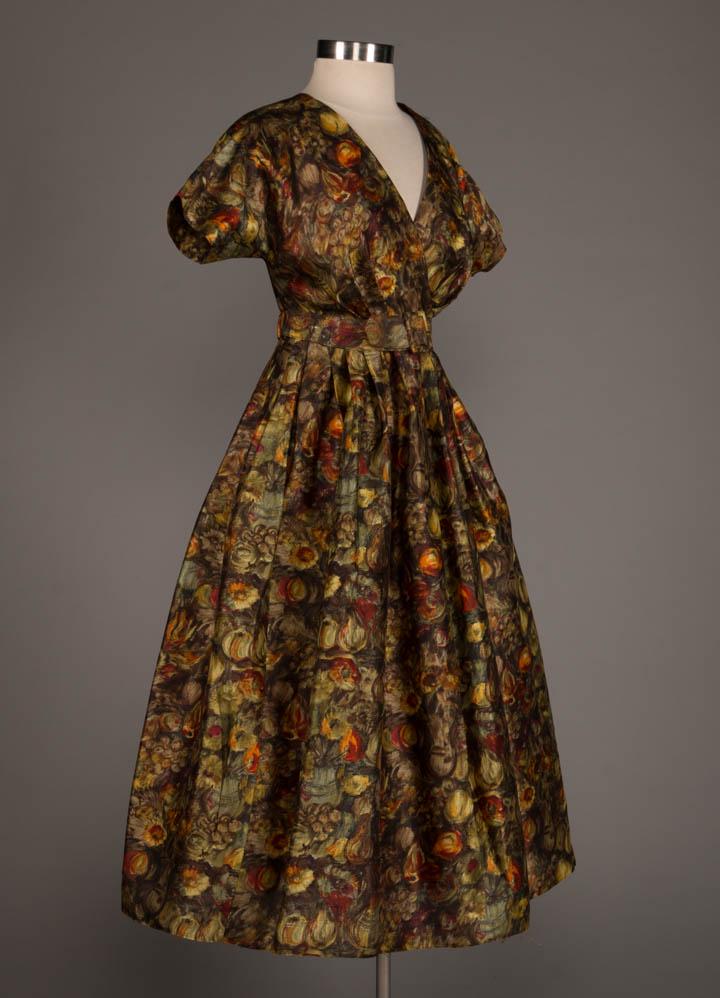 CLAIRE MCCARDELL SILK DAY DRESS, 1950s: Silk Degas inspired floral & fruit print day dress w/ cross over front closure to raglan short sleeve, knife pleated W, shaped self belt w/ elastized back, CF hook & eye closure, B 37", W 28", L 48.5"