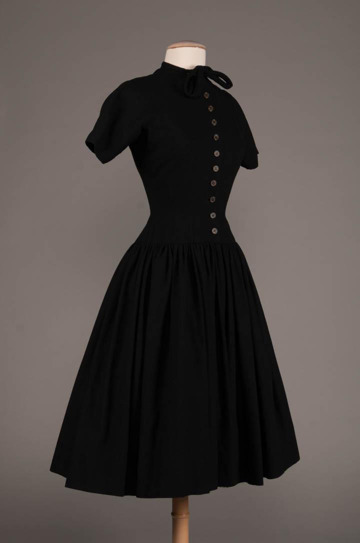 SISSY SPACEK WORN CLAIRE MCCARDELL DAY DRESS, AMERICA,: Black wool day dress shaped bodice to dropped W to gathered skirt, narrow collar to self tie bow, CF button closure, raglan w/ gusset sleeves, film worn Claire McCardell, worn by Sissy Spacek in "A Lo