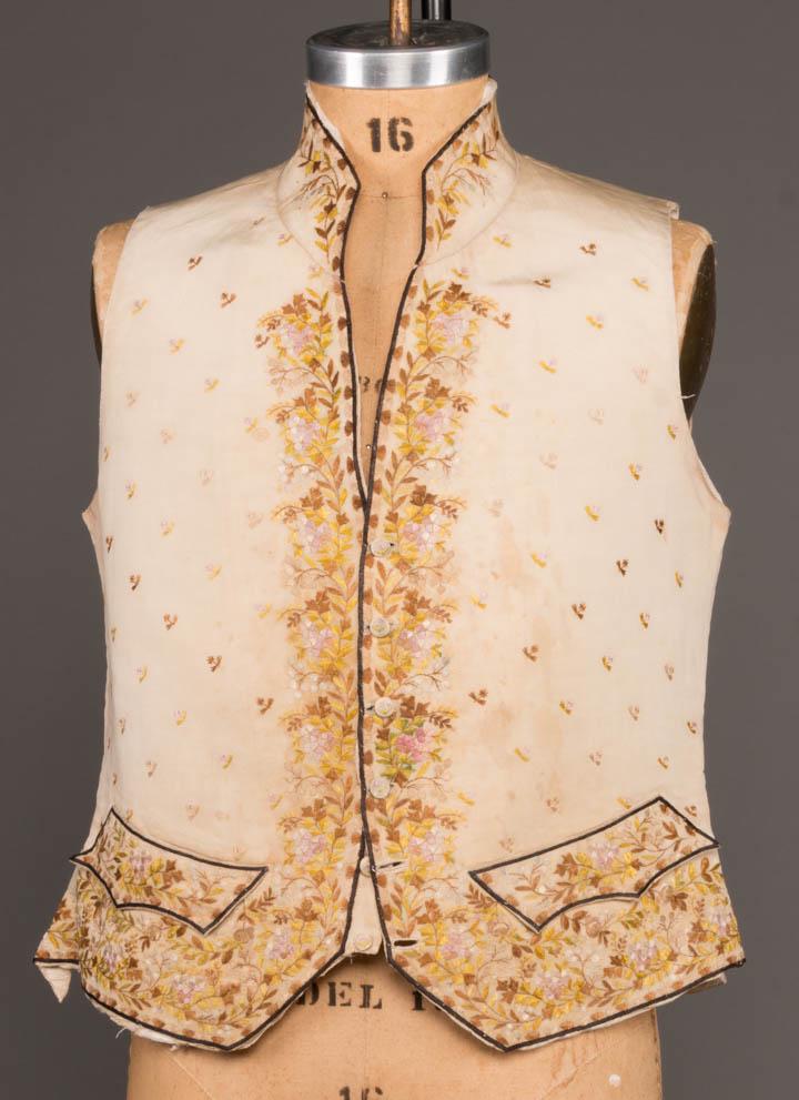 MANS EMBROIDERED WAISTCOAT, LATE 18TH C: Ivory ribbed silk embroidered w/ floral sprigs & foliage in muted greens, browns & pinks, miniature self-covered button closure at CF, two embroidered flap pockets at W, CH 40", L 21", (lining damaged