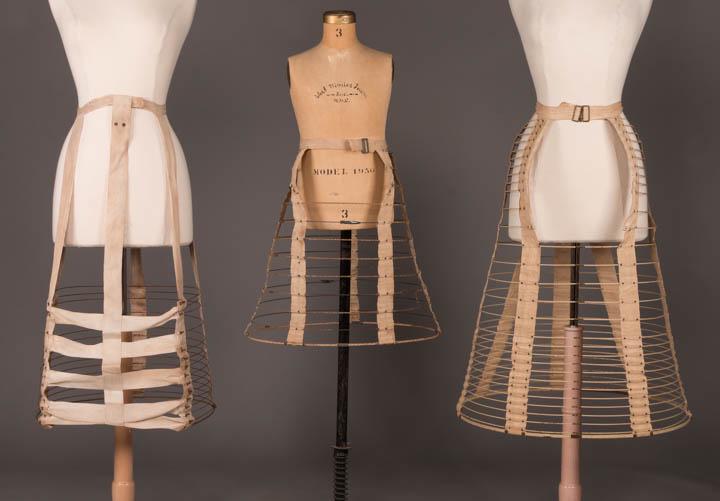 THREE BUSTLE CAGES, 1867-1880: 1 flat front w/ wide woven tapes to cage at back, 1870s, W 23.5-26", L 30", base circumference 59", (rusty, stained canvas, missing buckle); 1 child's w/ "Pat. 1867" on buckle, cotton covered watch sp