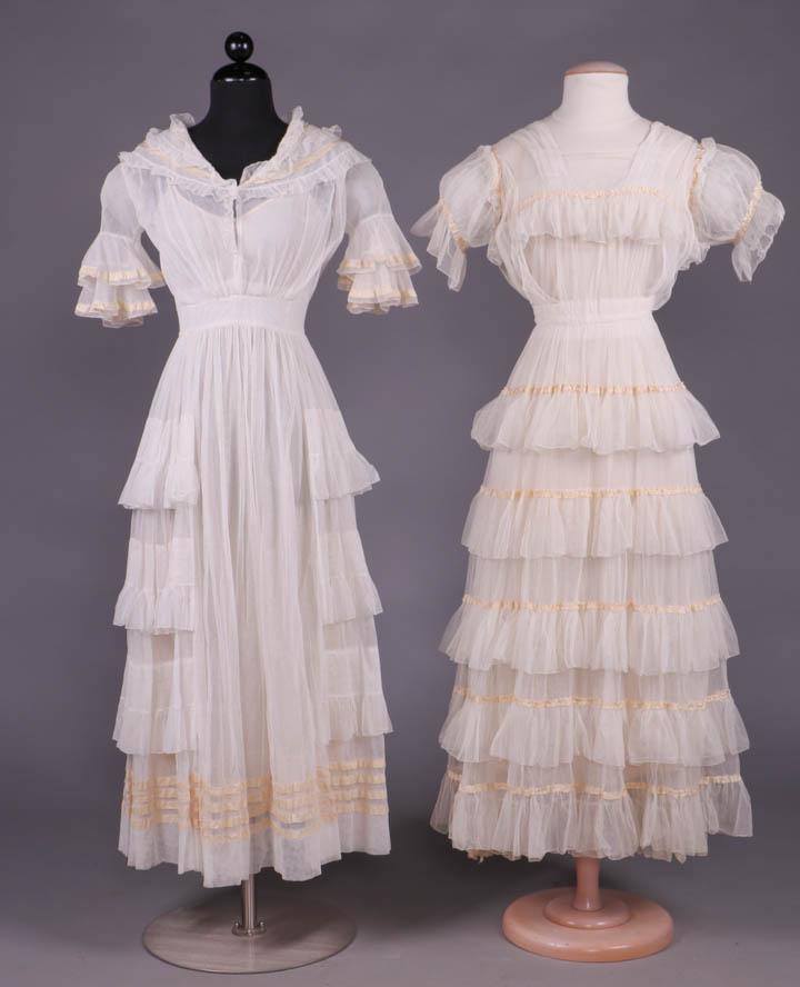 TWO NET & RUFFLE TEA GOWNS, 1910s: Both white cotton net: 1 w/ ribbon trimmed & ruffled deep collar ending in pennant point at CB, sleeves w/ double ruffled trimmed in gathered cream silk ribbon, ruffle edged panels inserted in horizon