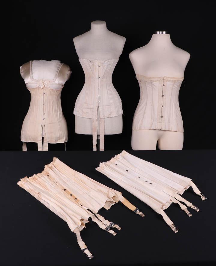 FIVE CORSETS, 1908-1915: 1 w/ lozenge lace trim & laces included, B 37", W 31", H 39.5", L 14"-15.5", (tiny-1.5" spot stains throughout, laces discolored & fraying); 1 w/ wide lace band & ribbon insertion, label "American Lad