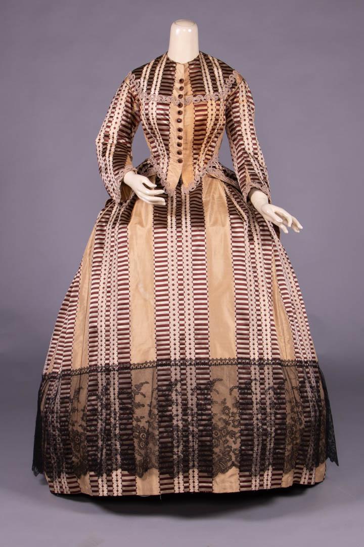 RIBBON PATTERNED SILK DAY DRESS, c. 1868: 4-pc gown of pale gold silk taffeta w/ warp patterned geometric & barred ribbon motif in silver & brown c/o casque bodice w/ pattern manipulated to enhance fitted bodice, cream silk passementerie in y