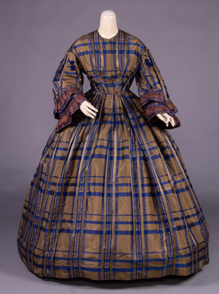 PLAID SILK TAFFETA DAY DRESS, c. 1858: 1-pc blue & brown complex ribbon plaid silk taffeta day dress, fitted bodice w/ CF closure, double box pleated sleeve into armscye & accented w/ blue passementerie drops & applied contrasting pleated 