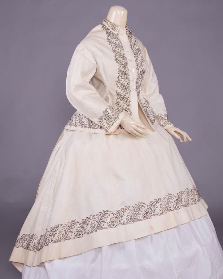 COTTON PIQUE GOWN ELEMENTS, c. 1866: 4-pc cream cotton pique ensemble c/o basque over jacket, bodice, overskirt skirt & belt w/ long tapered tails, all w/ military inspired two tone brown & white cotton & wool cord applied in gothic fron