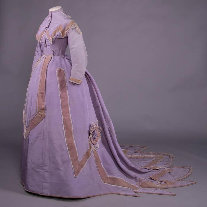 LAVENDER RIBBED SILK PRESENTATION GOWN, c. 1866: 2-pc trained ribbed silk lavender gown, fitted bodice w/ CF button closure, faux Van Dyke yoke trimmed in silk velvet bias bands & edged w/ fine silk lace, back w/ deep V double fold bias trim, armscy