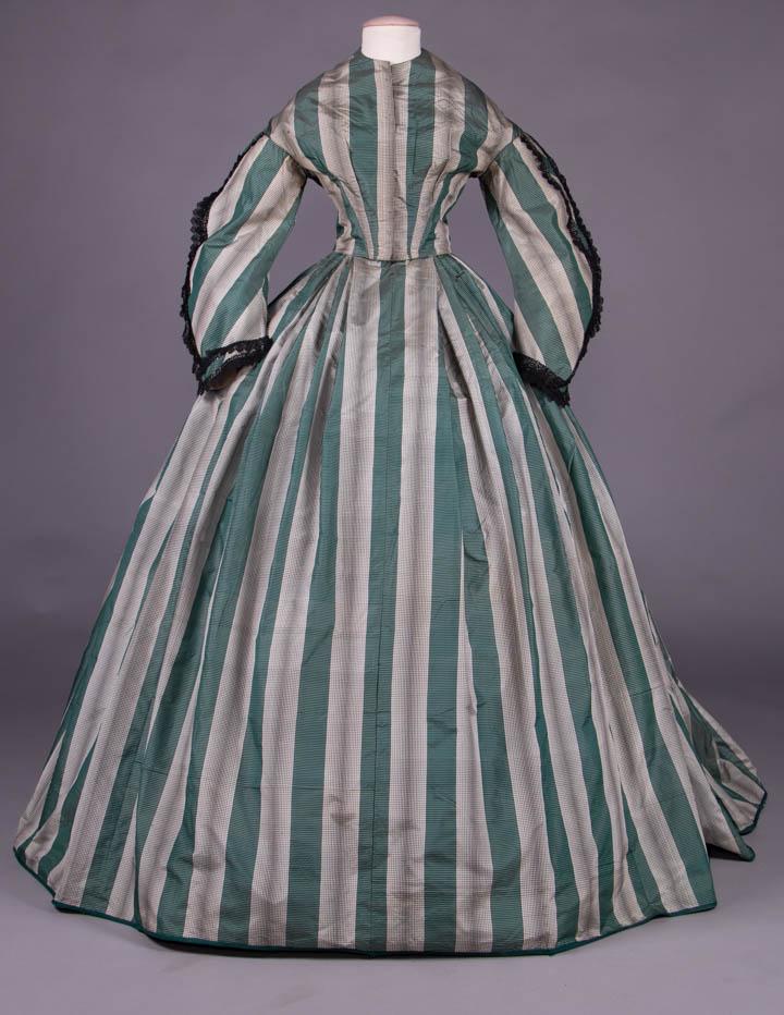 SILK TAFFETA DAY DRESS, 1860s: 2-pc silk taffeta gown in complex geometric broad ribbon stripe in black, white & green w/ fitted bodice, military shaped sleeve & cuff trimmed w/ black bobbin lace, piped neckline, armscye & hem of b