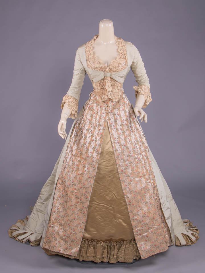 CELADON SILK FAILLE & LISERE EVENING GOWN, 1880s: Fitted bodice & princess line split skirt of lisere in entwined floral brocaded silk galloon motifs w/ deeply tucked blonde lace overlay to bodice front, neckline & engageante cuffs, extended celadon 