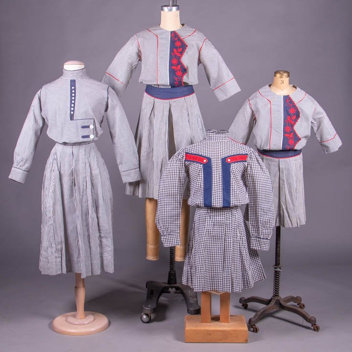 FOUR CHILDS SEASIDE COSTUMES, AMERICA, 1910s: 2 matching, both w/ drop W to box & knife pleated skirt, wide navy W band & CF w/ red detail & Schiffli embroidered florals, both w/ “Mandel Brothers” tags: 1 larger, CH 36", W 29", L 36.75", (1 m