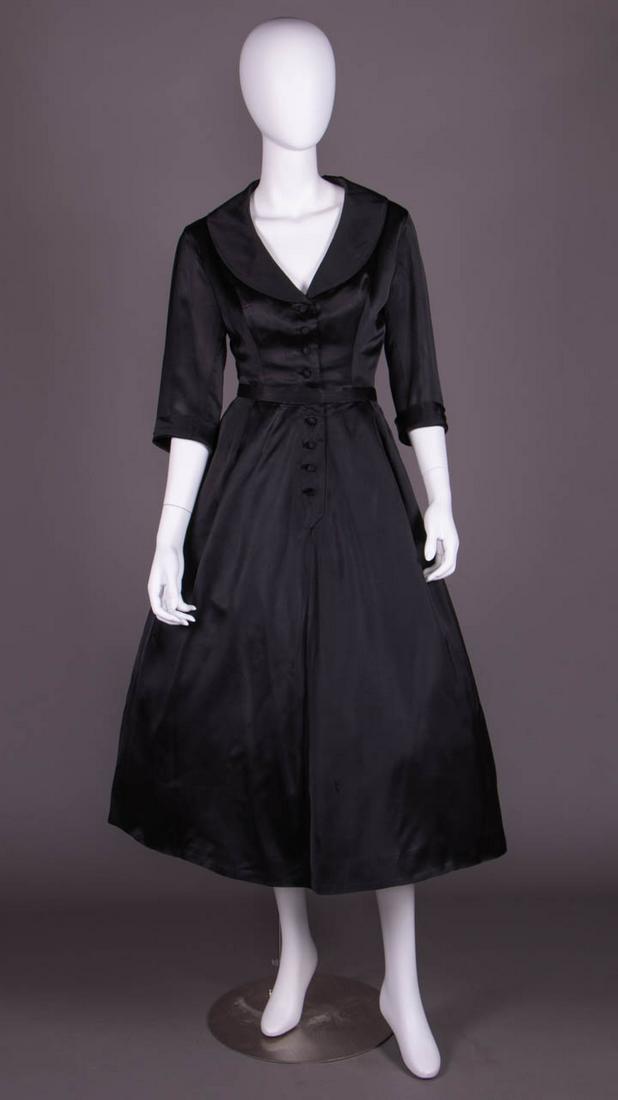 DIOR COUTURE DAY DRESS, LONDON, 1952-1954: 2-pc black silk satin dress c/o partially boned bodice w/ princess seam darts, shawl collar, CF self-covered dome button closures, elbow length cuffed sleeve, complex box & knife pleated skirt, attach