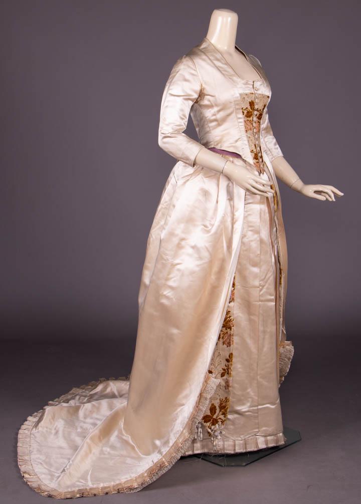 18TH C REVIVAL SATIN & CISELE VELVET GOWN, c. 1880: 3-pc cream silk satin & French cicele velvet gown w/ tromp l’eau band in lace & rose motif, fitted bodice w/ square neckline, fitted sleeves, faux stomacher cicele velvet at CF w/ thread covered