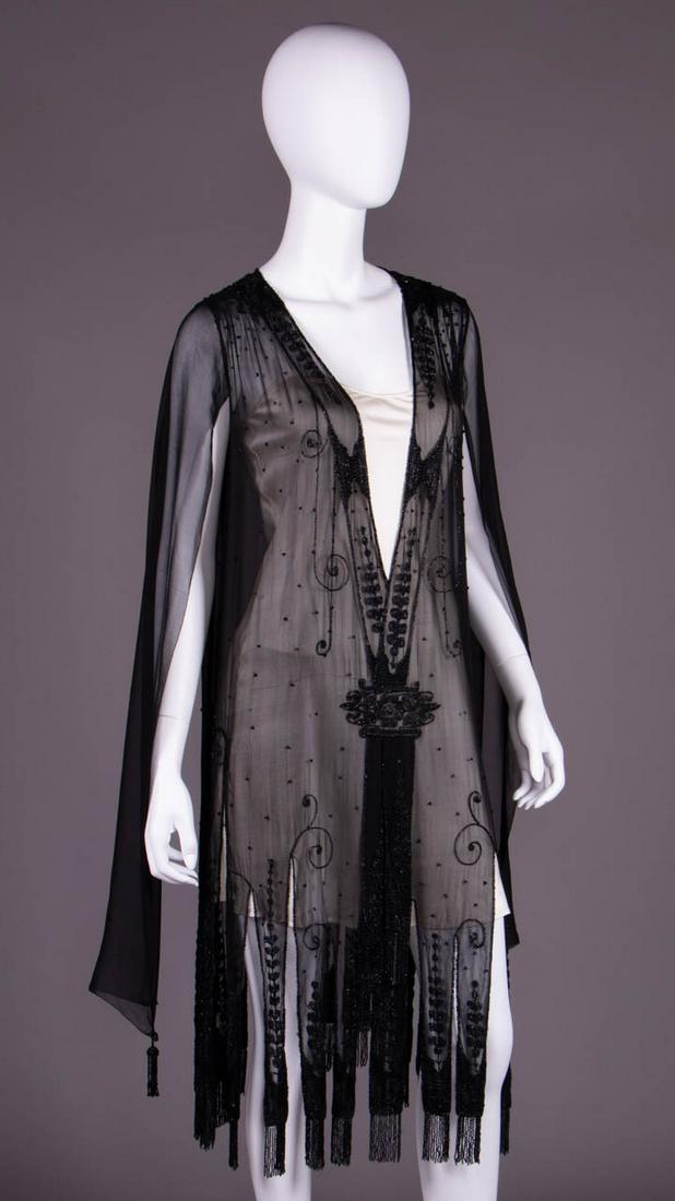 CHIFFON BEADED OVER DRESS, FRANCE, MID 1920s: Black Luneville beaded & embroidered chiffon overdress, deep V front w/ beaded band extending to hem, tabbed hem beaded & embroidered w/ stylized graduated bud stock motif & beaded fringe, vestigial s