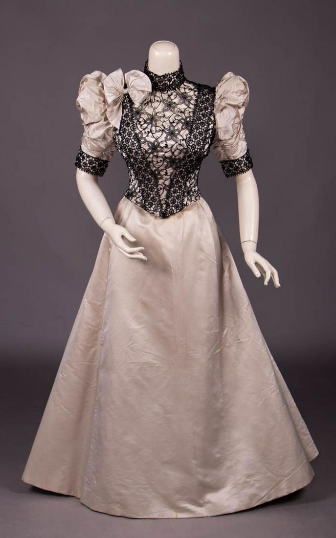 BONE SILK SATIN EVENING GOWN, c. 1893: 2-pc bone twill silk satin gown, silk organza & chemical lace bodice overlay w/ inserted bands of French jet beading on reticella inspired black corded grid, also to stock collar & cuffs, self bow at 