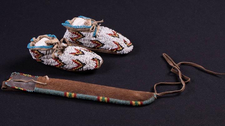 CHILD'S MOCCASINS & BEADED KNIFE SHEATH, LAKOTA SIOUX: 1 pair deerskin child's moccasins w/ squaw stitch embroidered bead work w/ sinew construction, Lakota (Western Sioux) c. 1900, Wd 2", L 4.5", Ht 2", (worn, suede dirty) excellent; 1 knife sheath sinew