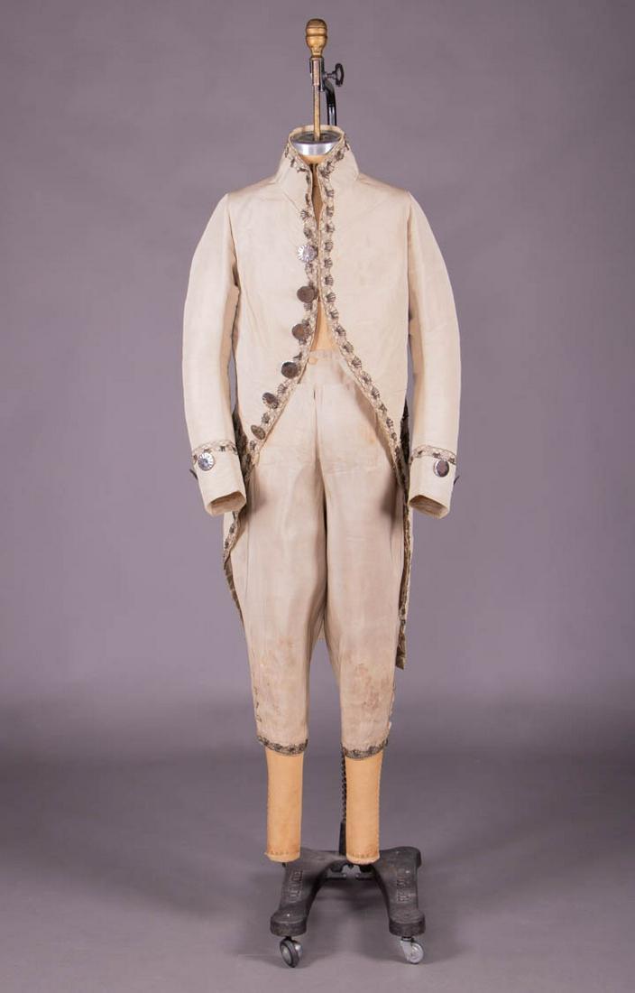 MACARONI STYLE FANCY DRESS, LATE 18TH C: Bone silk faille mans ensemble c/o cutaway coat w/ high standing collar, decorative applied H pockets, CF opening, sleeve cuffs, pockets, flaps & CB timed w/ silver bobbin lace, CF, sleeve & CB w/ lar