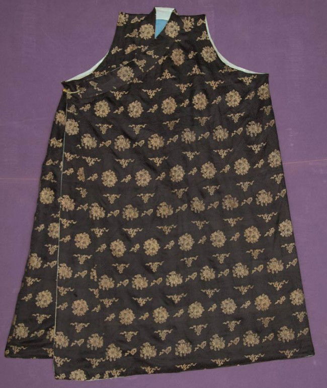 BHUDDIST CHUBA, TIBET, 19TH C: Black maze pattern silk damask brocaded w/ metallic gold flowers & auspicious symbols, sleeveless, right side single brass button closure, blue cotton lining, CH 62", L 52", excellent.