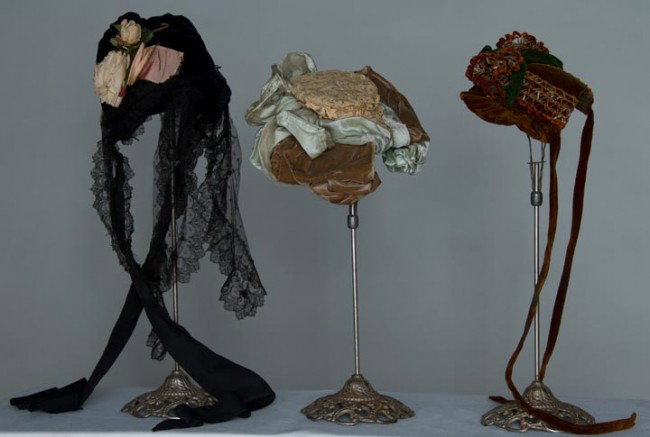 THREE SMALL VELVET BONNETS, 1890s: 1 midnight blue w/ black lace & pink cloth flowers; 1 cocoa brown & celadon green, cream lace covered crown & 4 oval rhinestone buckles in front; 1 rust w/ trims in open work straw, rust chennile & fo