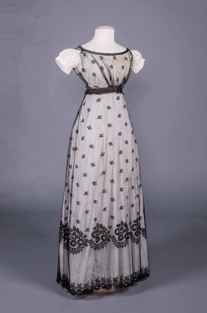 LACE RUN EMBROIDERED NET OVERDRESS, c. 1820: Black net overdress w/ lace run motifs, double piped bias satin neckline, cartridge pleated CB, B 45", W 24", L 52", (underdress & petticoat N/I, sleeves removed & armscyes raw, some pleats undone CB 