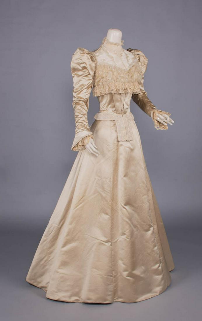 PEAU DE SOIE EVENING GOWN, 1890s: 2-pc cream silk peau de soie evening gown w/ watered silk stock collar, plastron front yoke, cuffs & W band w/ front tabs embellished w/ crystal seed beads, silvered crystal beads & faux pearls, openw