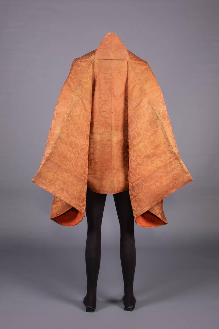 BUDDHIST MONKS HAORI, JAPAN, 1780-1850: Buddhist monk's haori of orange twill weft patterned silk w/ stylized mon & scrolling florals, lined w/ starched cotton, CH 60", L 34", (general fading/discoloration, lining stained, panel added at CB