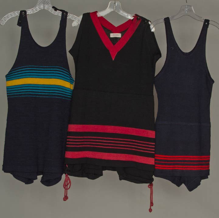THREE WOOL KNIT SWIM SUITS, AMERICA, 1915-1920s: All w/ attached skirt over short leggings, each w/ U.S. label: 1 black w/ red knit V-neck & skirt stripes, bloomer under leggings w/ red laces, (moth damage); 1 navy w/ red striped skirt; 1 navy w/ tu