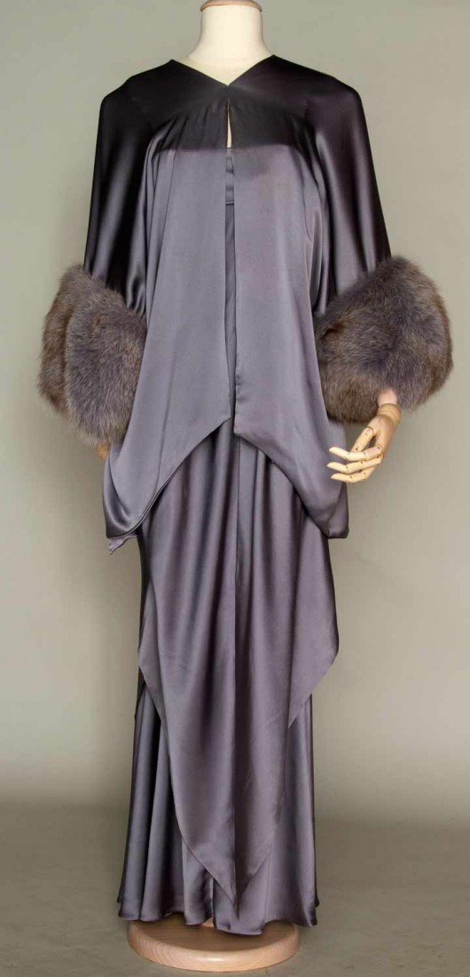 TRIGERE SILK EVENING ENSEMBLE, 1974: Grey charmeuse gown & jacket, labeled, strapless gown, hankerchief CF & CB point over grey silk under-skirt, shaped jacket w/ cowl back & slit sides, 3/4 L sleeves trimmed in grey fox fur, B 36", H 39
