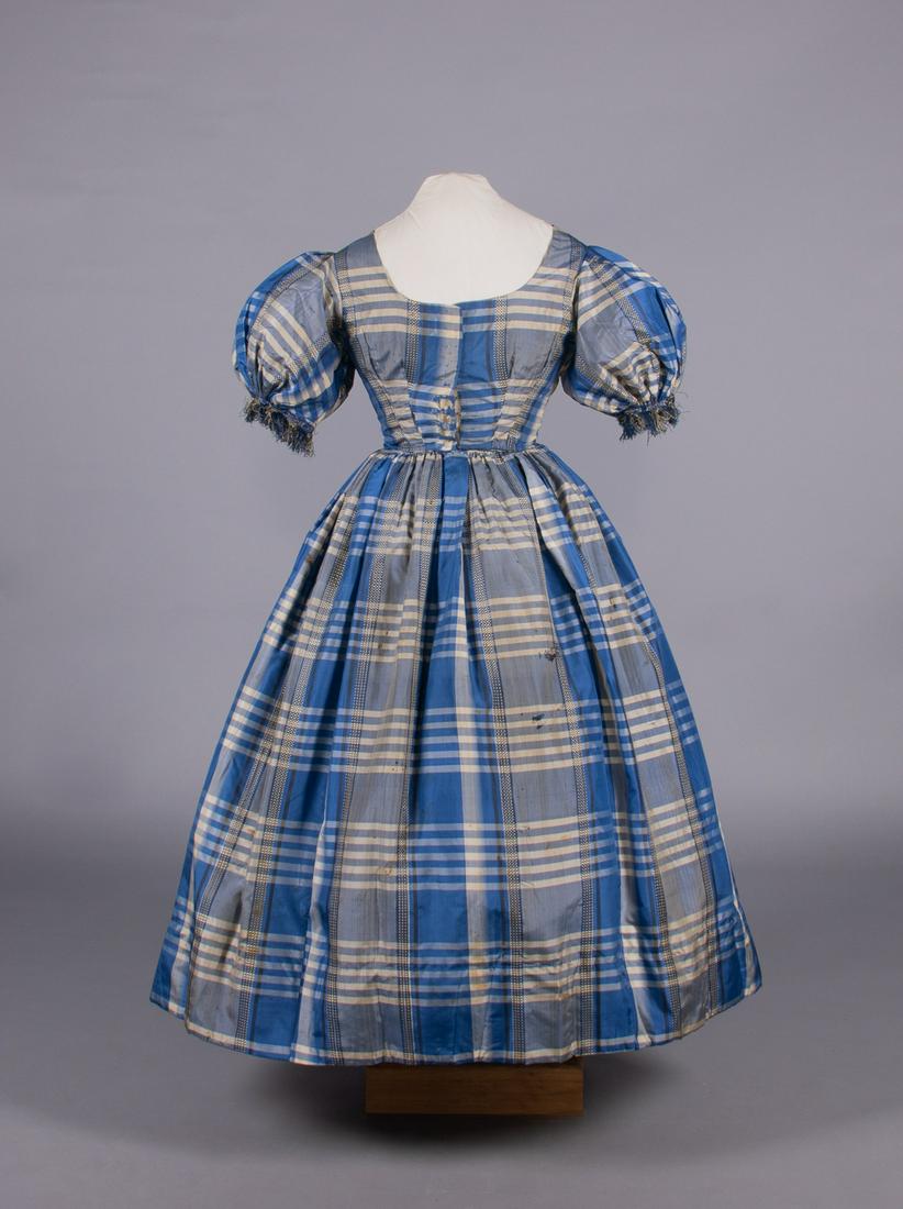 GIRLS SILK TAFFETA DAY DRESS, 1850s: Plaid silk taffeta w/ checkerboard ribbon stripe, woven silk fringe trim to puff sleeves, CF hook & eye closure, lined in linen & silk, CH 32.5", W 23", L 46", (shattering CF bodice & underarms, many