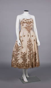 CEIL CHAPMAN SILK & LACE EVENING DRESS, AMERICA, 1950s: Cream silk satin strapless evening dress w/ appliquÃ©d brown guipure floral lace motifs, fitted bodice, pleated W band into flat bow at CB, full knife pleated skirt, integrated tulle petticoat, labe