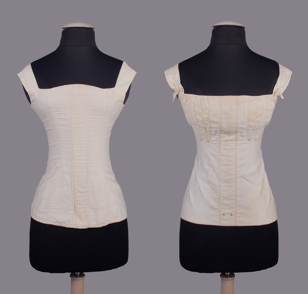 TWO COTTON CORSETS, 1830-1840s: 1 white cotton corset w/ back stitch silk embroidery, bone eyelets attached to edge of CB opening, interior side French seams, stamped “Emily J. Davis”, B 28”, W 22”, H 30”, 