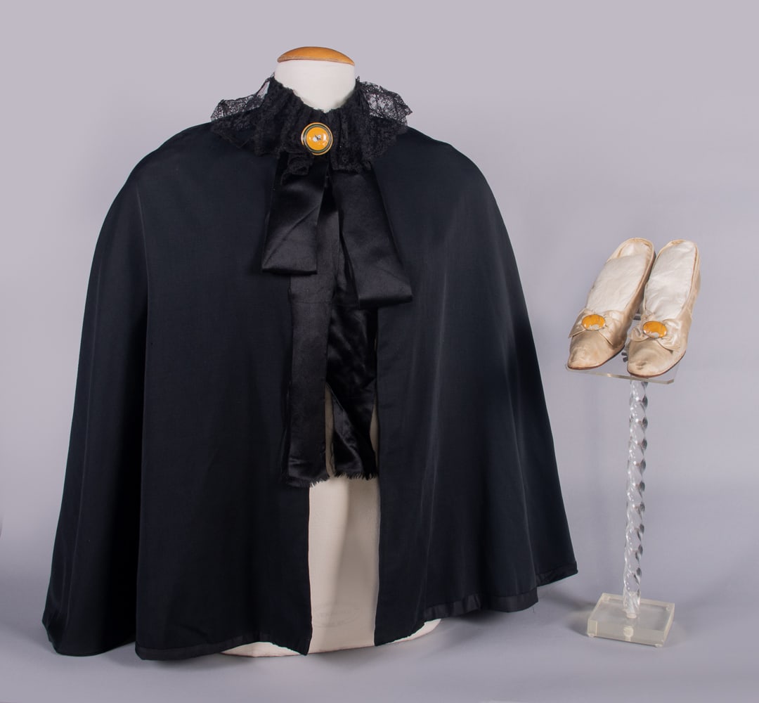 WIENER WERKSTATTE EVENING PUMPS & CAPE, 1910s: 1 black silk crepe cape w/ silk satin ribbon, black tulle lace, domed floral motif enamel shanked button at throat closure, L 32”, (buckle chipped w/ wear/scratches, minor tarnish, lace collar u