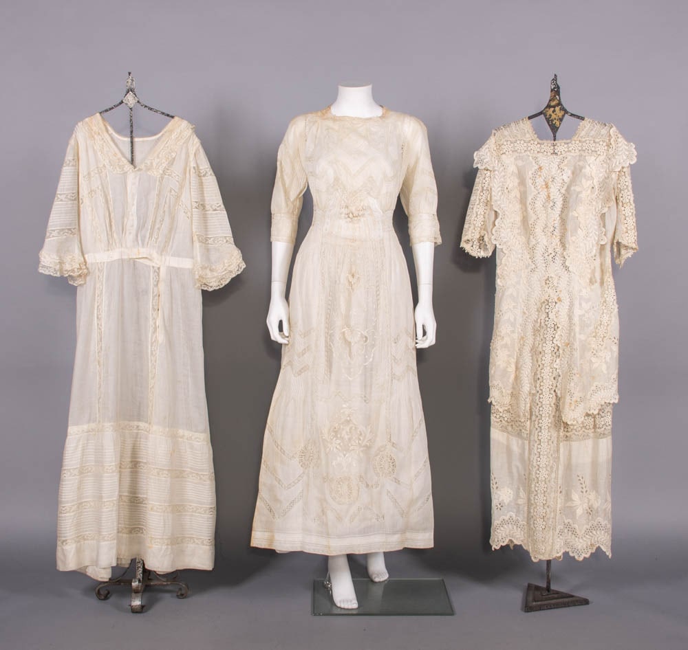 THREE COTTON LINGERIE DRESSES, c. 1912-1914: 1 dress of off-white cotton w/ filet & bobbin lace insertion & hand embroidery, crochet petal & ball fringe to CF bodice, c. 1912; 1 dress of off-white cotton trimmed w/ mm lace insertions & pin-tucks