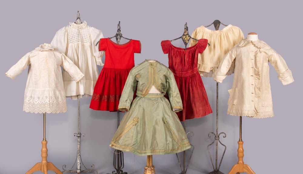 SEVEN CHILDREN’S DRESSES OR UNDERGARMENTS, 1850-1894: 1 white cotton w/ smocking & mm embroidery, c. 1880, B 24”, L 19”; 1 white cotton w/ cutwork yoke, c. 1894, B 20”, L 21”; 1 red merino wool w/ silk braid, 1850s, B 18”, L