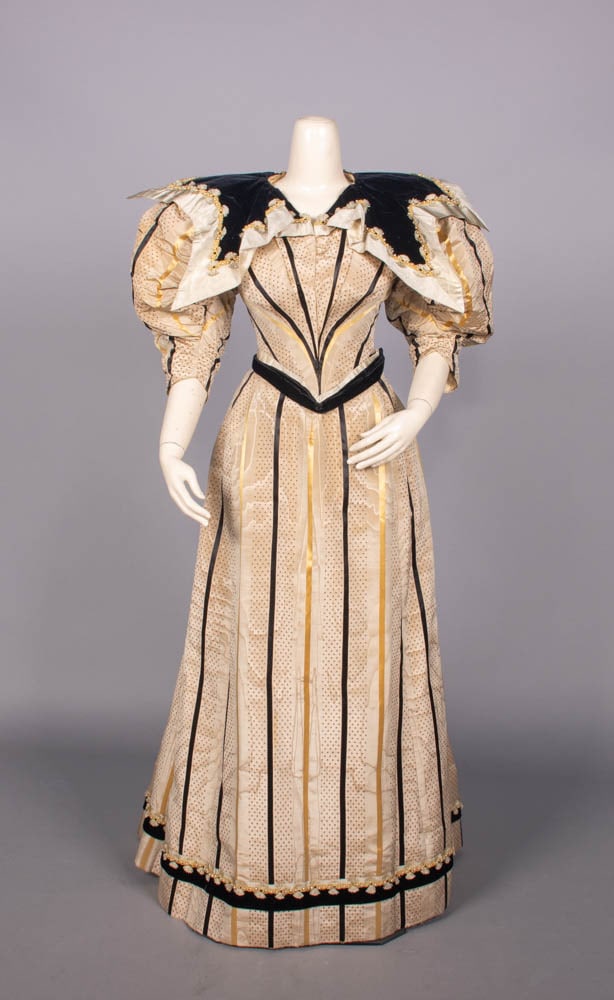 RIBBON STRIPED SILK MOIRE AFTERNOON GOWN, c. 1895: 2-pc tan, black & yellow ribbon striped silk moire overprinted w/ miniature samara motif, black silk velvet shaped SH panels & narrow W w/ pearl embroidered cord & cringed fringe trim, label “A. Cow