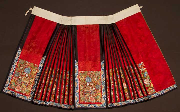 EMBROIDERED RED SKIRT, CHINA, 19TH C: Dark red silk damask, virtuoso embroidery on center squares & in side pleats, figures, flowers, auspicious symbols, bats, birds & fish worked in several stitch patterns, each element outlined in gold 