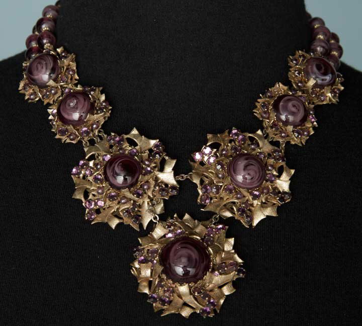 HASKELL PURPLE JEWELED NECKLACE, 1940-1950s: 3 pair & 1 center drop, each brass floral blossom hand set w/ large marbled purple glass cabuchons & purple rhinestones, Miriam Haskell stamped in oval under clasp, L 15.5", excellent. From Estate of