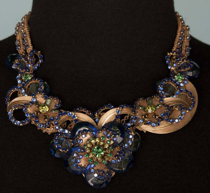 HASKELL BLUE JEWELED NECKLACE, 1940-1950: 2 strand brass chain, center brass leaves & blossom embellished w/ large succrette stones & tiny rhinestones in green & blue, Miriam Haskell stamped in oval under clasp, L 16.5", (blue rhinestones mis