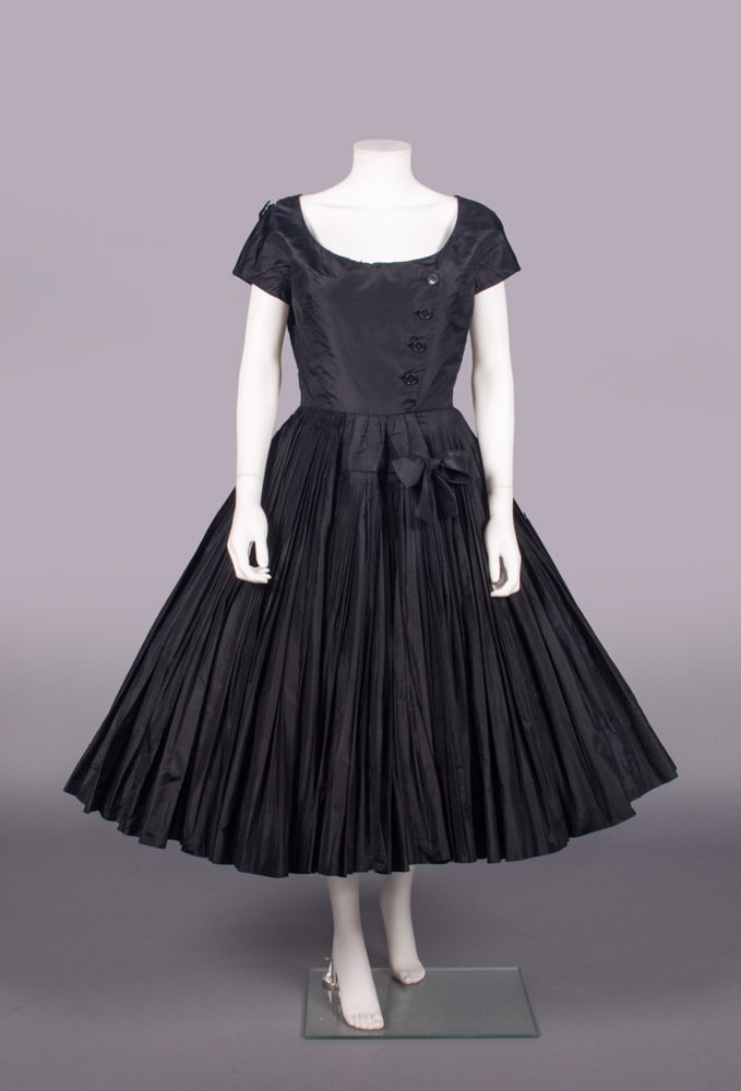 GALANOS SILK TAFFETA PARTY DRESS, USA, 1952-1955: Black silk taffeta party dress w/ scoop neckline, short sleeves, decorative buttons to left bodice front, finely knife pleated very full calf length skirt, 1952-1955, label “Galanos Originals, Bever