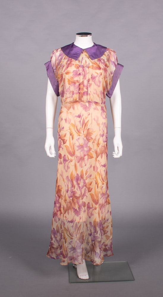 PRINTED SILK CREPE GARDEN PARTY DRESS, EARLY-MID 1930s: Silk floral crepe chiffon party dress w/ purple taffeta trim to collar & sleeve, gathered stitching around yoke, peach silk satin slip, B 38”, W 28”, L 48”, slip B 38”, (trim f