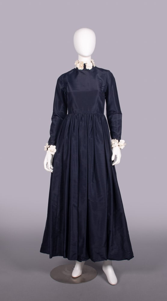 BILL BLASS TAFFETA & CAMELLIA FLOWER EVENING GOWN, 1970s: Navy silk taffeta gown w/ long sleeve, band collar over open back, detachable stiffened cloth camellia choker & cuffs, label “Bill Blass”, 1960s, B 34”, W 26”, L 56”, (few lo