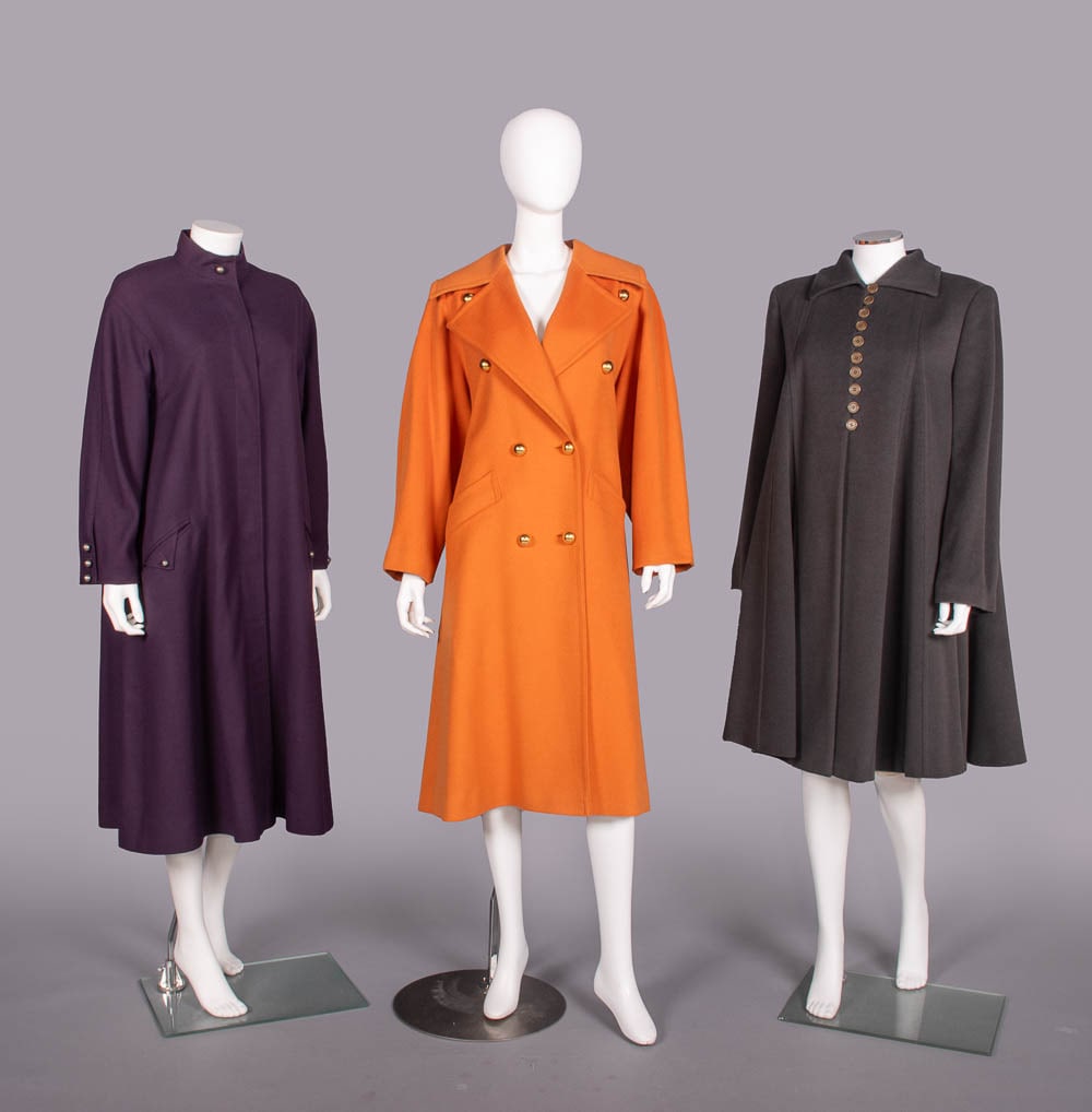 THREE DESIGNER WOOL OR CASHMERE COATS, PARIS & MILAN, 1980-1990s: 1 purple wool twill coat w/ band collar, silver ball buttons & logo lining, label "Louis Feraud, Paris", B 42", L 46", (minor wear) excellent; 1 orange wool & cashmere blend trenchcoat w/ tie belt & g