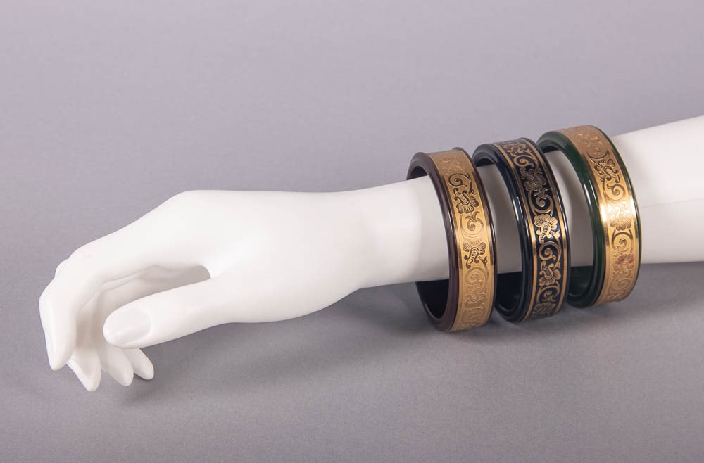 THREE MARLOW COSMETIC BAKELITE BRACELETS, PARIS, 1920s: 3 marked "Marlowe Cosmetic Bracelets, Parisienne", circ 8", Wd 0.75", 1 brown (applicators missing), 1 black & 1 green (missing 1 mirror & 1 applicator, slider stiff, minor residue) (all w/ mirrors cl