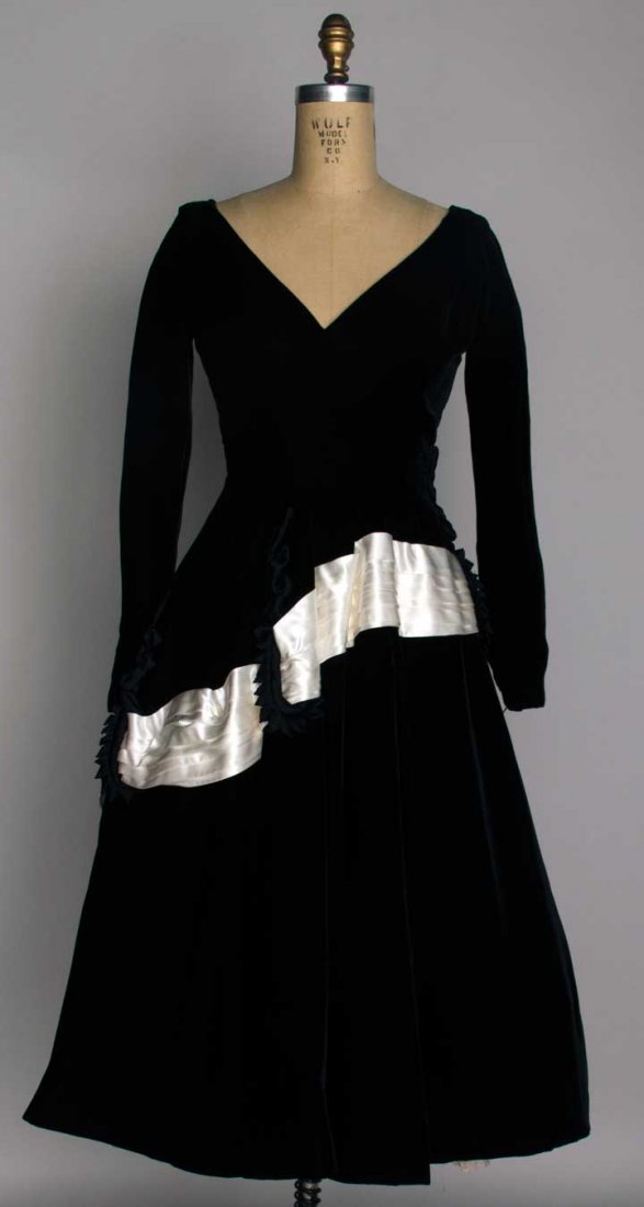 OLEG CASSINI DEADSTOCK EVENING DRESS, c. 1955: Black velvet, fitted bodice w/ sweetheart neckline, full skirt, white satin sash, labeled & original hang-tags w/ $139.95 price, B 36", W 27", L 47", excellent.