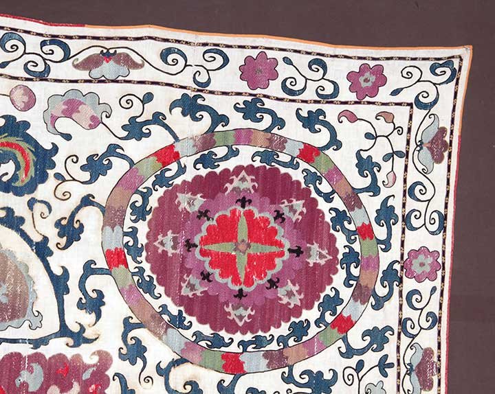EMBROIDERED SUZANI, CENTRAL ASIA, 19TH C: White cotton ground, flower head & pinwheel embroidery patterns in mauve, red & blue cotton floss, 8 vertical pieced strips, 96" x 164", (mends, losses & fading) very good, t/w 1 coral, gold & blue su