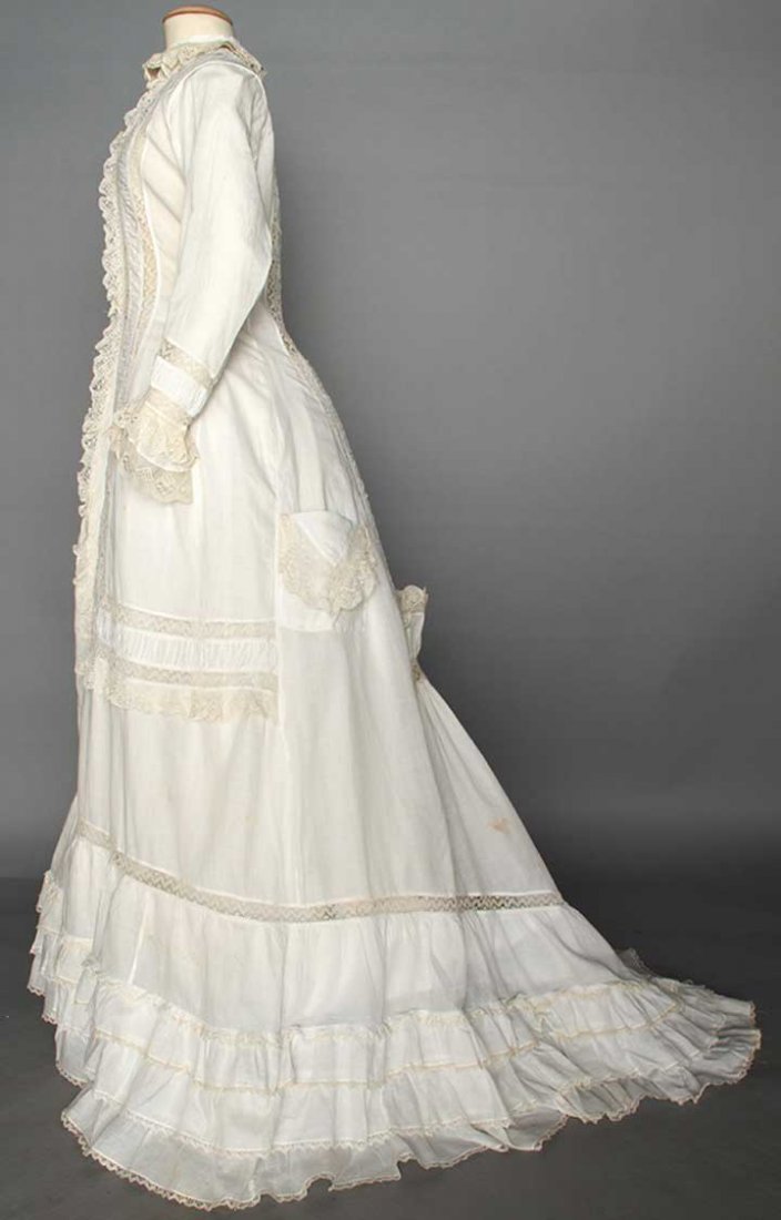 WHITE COTTON MORNING DRESS, 1870s: 1-piece, princess lines, trimmed w/ cream bobbin lace, low bustle back, CF thread-covered buttons, side pockets, trained & ruffled skirt, B 32", W 25", CF L 57", CB L 70", (few brown stains, couple pi