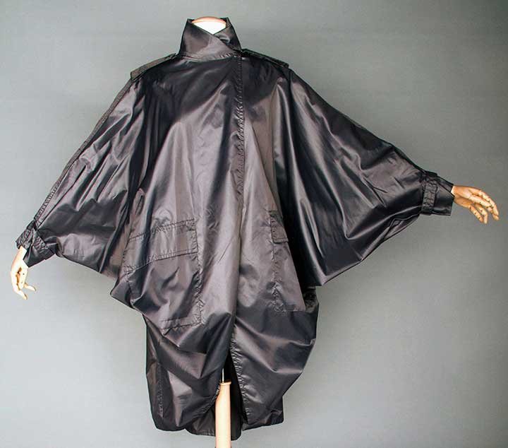 ISSEY MIYAKE RAIN CAPE, 1990s: Silver-gray w/ metallic sheen, 3/4 length, batwing sleeves, high stand collar, patch pockets, self fabric epaulets, 2 woven labels: "Issey Miyake" & "Henri Bendel", L 49", excellent.