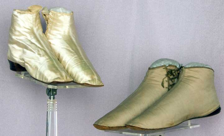 TWO PAIR LADIES' SIDE LACED ANKLE BOOTS, 1840-1860: Both pair straights w/ square toes & original laces: 1 pair white silk satin w/ knock-on wooden heel, (faint green stains on vamps) very good; 1 pair taupe cotton & wool flats w/ black patent leather