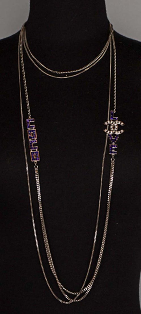 CHANEL SILVER NECKLACE, c. 2000: 5 silver chains, 2 at collar bone & 3 long, to navel, graduated in size, 2 purple jeweled elements on either side of long chains, 1 spells COCO & 1 spells LCCOVE, small fob marked "Chanel" & "CC", L 5