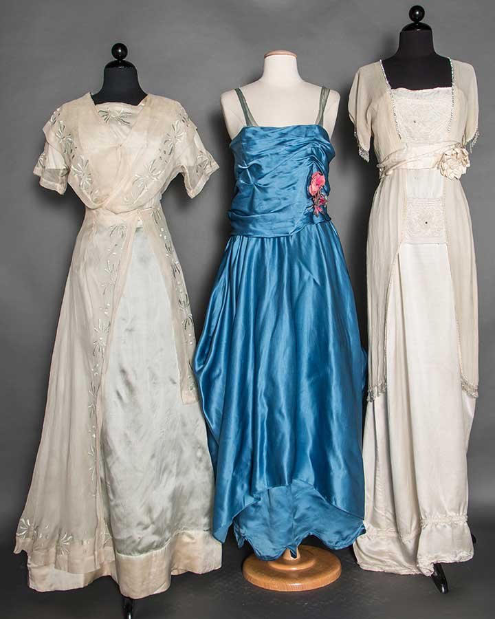 THREE EDWARDIAN EVENING GOWNS, c. 1912: 1 blue satin w/ pink cloth flowers, B 36", W 26", L 56", (silk net shoulder straps damaged, light underarm stains) fair; 1 ivory chiffon over silk satin, crystal bead & rhinestone trims, label "Slagy 
